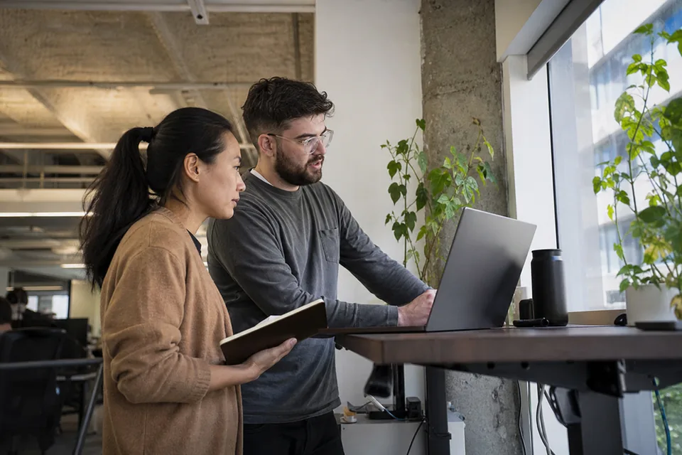 QA engineer and product manager reviewing an answer together at a standing desk in an open office